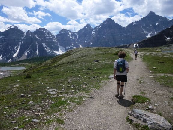 hikers follow a trail with mountain peaks in background