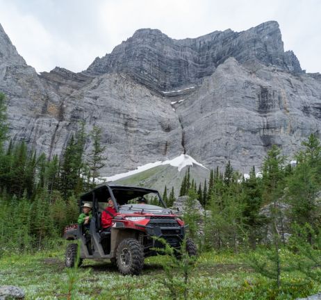 Hikers board ATV with mountain peaks in background